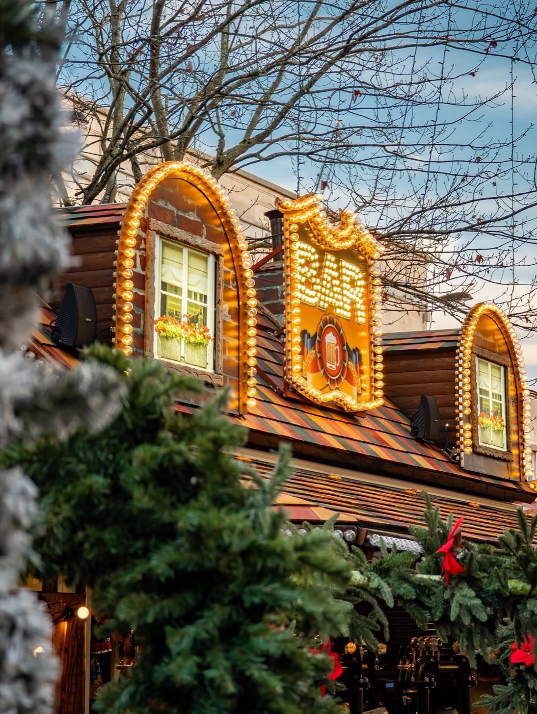 A warmly lit wooden market chalet glowing at night with snow on the roof